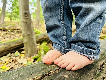 Foto mit nahaufnahme von Kinderfüßen, die barfuß auf einem liegenden Baumstamm stehen